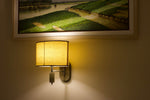 Warm glow of a wall lamp lighting up a serene landscape painting in a cozy indoor setting.